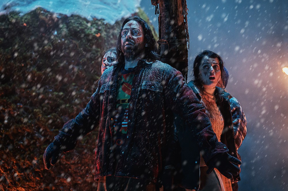 In the snow three people look worried about something the camera can't see