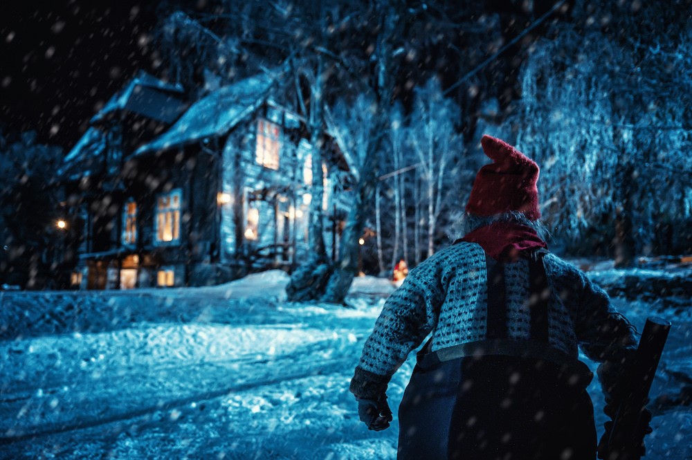 Image shows it snowing with a small creature looking toward a house