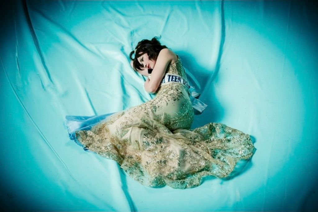 Woman in gold dress laying on blue sheet. Image from the film Other